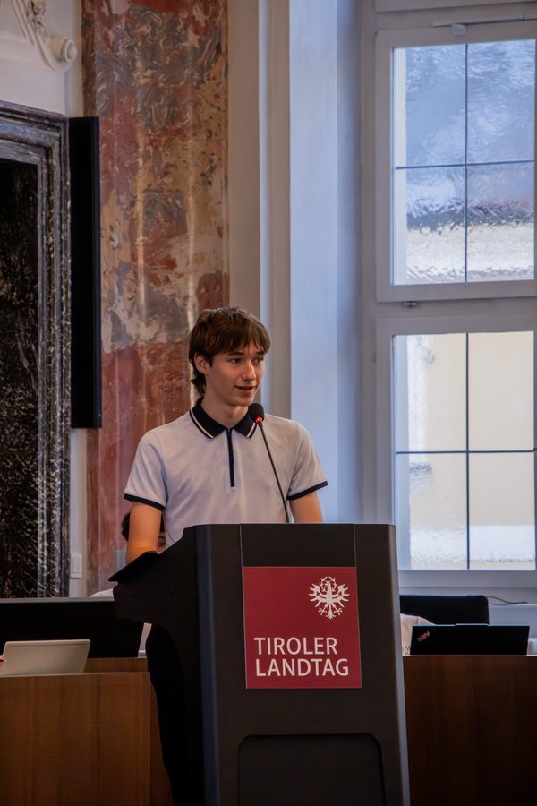 Sandro Exenberger am Rednerpult des Tiroler Landtags vor einem hellen Fenster